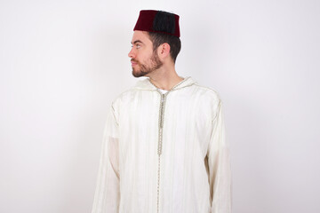 Side view of young happy smiling young handsome Caucasian man wearing Arab djellaba and Fez hat over white wall