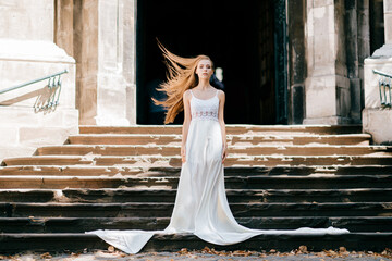 Young romantic elegant girl with flying hair in long white dress posing on the stairs of ancient palace