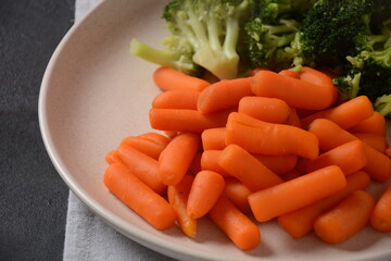 Bunch of cooked small boiled carrots and broccoli  on white plate. Healthy eating