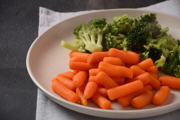 Bunch of cooked small boiled carrots and broccoli  on white plate. Healthy eating