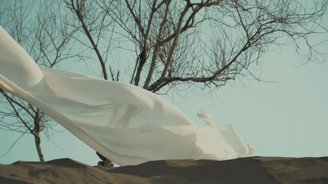 a View of long white fabric shawl at sand dune, like sails fluttering in wind. Concept of femininity, tenderness, freedom.