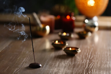 Incense stick smoldering on wooden table in room. Space for text
