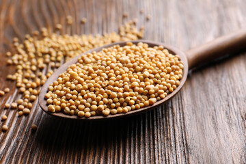 Mustard seeds in spoon on wooden table, closeup