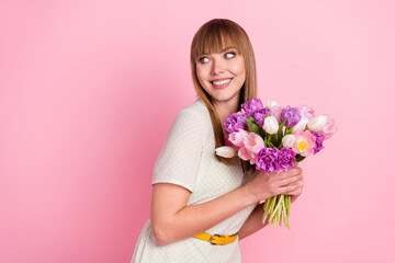 Portrait of attractive cheerful glad girl holding in hands flowers looking aside copy space isolated over pink pastel color background