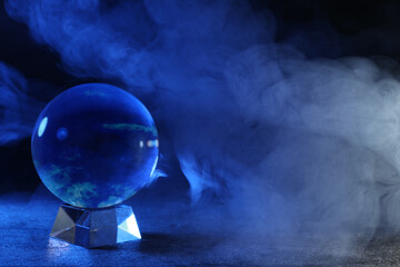 Magic crystal ball on table and smoke against dark background, space for text. Making predictions
