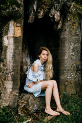 Young attractive barefoot blonde girl in blue romantic dress sitting in the old tree