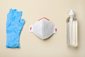 Medical gloves, respiratory mask and hand sanitizer on beige background, flat lay