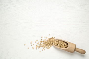 Soya beans with scoop on white wooden table, top view. Space for text
