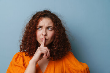 Displeased ginger young woman showing silence gesture