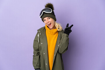 Skier Russian girl with snowboarding glasses isolated on purple background smiling and showing victory sign