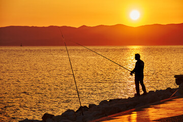 Fisherman silhouette on the beach at sunset