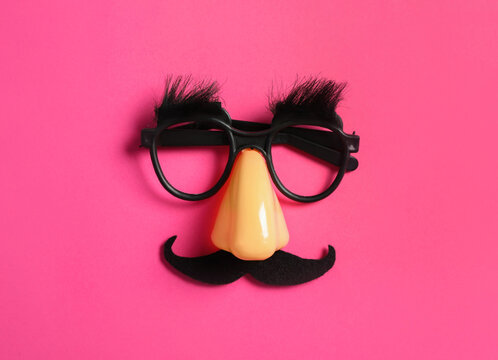 Funny glasses on pink background, top view