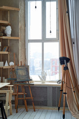 The artist's light workshop with large light windows. An old big lamp on a tripod. Shelving with plaster forms, easels.