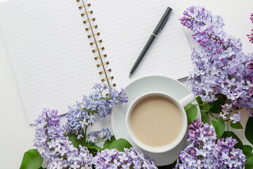 spring composition flat lay white cup of coffee, violet beautiful bouquet of lilacs, notebook, pen, concept of spring and comfort 