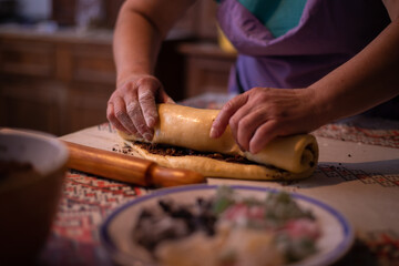 Obraz premium housewife rolling the dough filled with sweet ingredients to be placed in the oven tray. a traditional homemade cake recipe known as cozonac