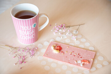 Handmade chocolate with fresh and dried fruits and cup of hot tea on light wooden table with flower