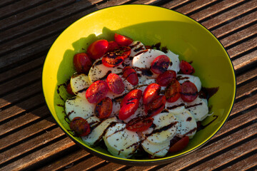 Delicious caprese salad with ripe cherry tomatoes on a wooden table in a green bowl