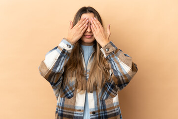 Young caucasian woman isolated on beige background covering eyes by hands