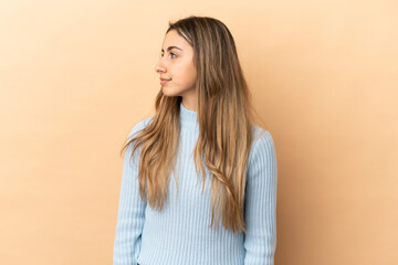 Obraz premium Young caucasian woman isolated on beige background looking to the side