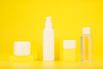 Set of cosmetic bottles with yellow geometric props against bright yellow background. Concept of skin care and beauty products with sunscreen