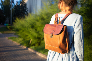 Girl in blue dress wears leather fashion handmade bag. Leather backpack craft product.