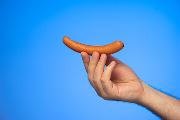 Raw Frankfurter wurst held in hand by Caucasian male hand isolated on blue background