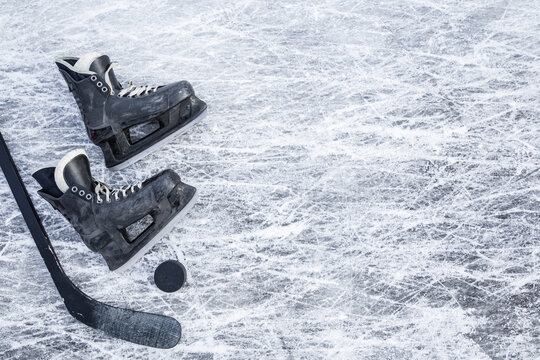 Old scratched black hockey male skates, stick and rubber puck on ice background. Closeup. Empty place for text. Top down view.