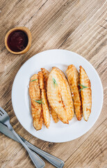 Baked potato fries with sea salt and rosemary on a rustic wooden background.