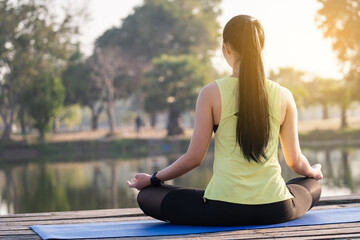 Fototapeta na wymiar Young Asian beautiful woman practicing yoga and meditate in the lotus pose outdoor beside the lake in the morning for relaxation and peace of mind. Harmony and meditation concept. Healthy lifestyle