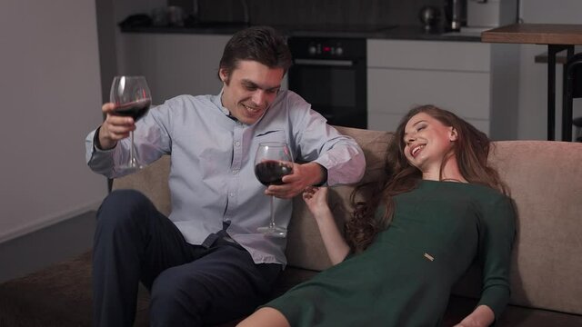 A couple of lovers at home, drinking wine. The man seduces the woman in the room.