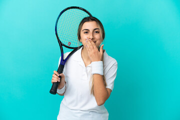 Young woman tennis player isolated on blue background happy and smiling covering mouth with hand