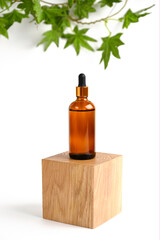 Cosmetic in a glass bottle on wooden podium, green leaves on white background.