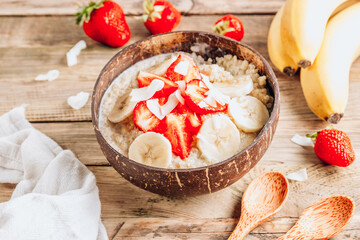 Quinoa porridge with coconut milk and fresh strawberries in a coconut bowl wooden rustic background. Healthy Lactose and Gluten Free Breakfast.