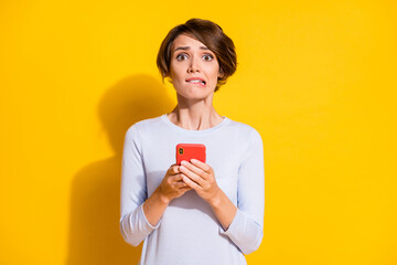 Photo of nervous anxious lady hold telephone bite lip wear white shirt isolated yellow color background