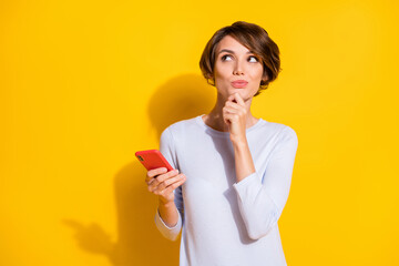 Photo portrait of minded girl looking at blank space holding phone in one hand isolated on bright...