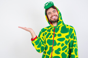 young caucasian man wearing a pajama standing against white wall smiling cheerful presenting and pointing with palm of hand looking at the camera.