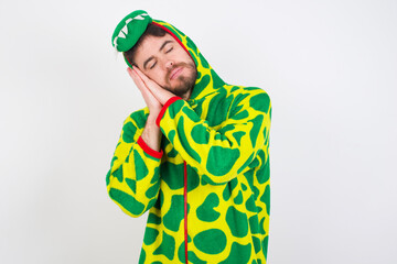 young caucasian man wearing a pajama standing against white wall sleeping tired dreaming and posing with hands together while smiling with closed eyes.