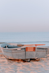 Fototapeta na wymiar Boat with a paddle on a sandy beach by the sea. Close-up, at dawn. Photography in pastel tones and Vertical photos