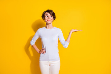 Photo portrait of woman holding blank space in hand isolated on bright yellow colored background