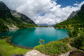 Summer sunny day in nature. Panoramic view of Aviolo lake in Adamello park, Italy. Vivid turquoise color water in alpine mountain lake sandwiched between mountains.