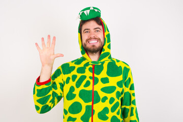 Fototapeta premium young caucasian man wearing a pajama standing against white wall showing and pointing up with fingers number five while smiling confident and happy.
