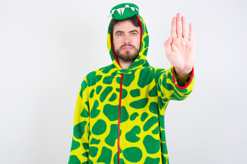 young caucasian man wearing a pajama standing against white wall doing stop sing with palm of the hand. Warning expression with negative and serious gesture on the face.