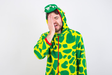 Fototapeta premium young caucasian man wearing a pajama standing against white wall Yawning tired covering half face, eye and mouth with hand. Face hurts in pain.