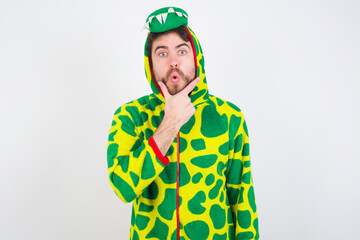 young caucasian man wearing a pajama standing against white wall Looking fascinated with disbelief, surprise and amazed expression with hands on chin
