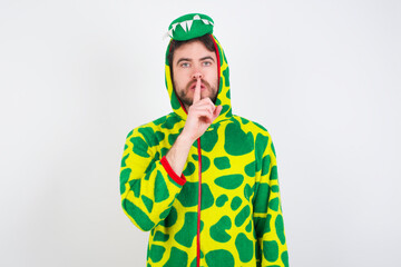 Fototapeta premium young caucasian man wearing a pajama standing against white wall makes silence gesture, keeps finger over lips. Silence and secret concept.