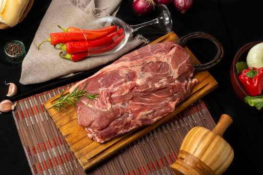 pork in a piece, cut bondiola on a table with vegetables rustic napkin pepper.