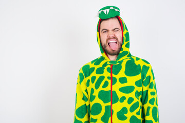 Fototapeta premium young caucasian man wearing a pajama standing against white wall sticking tongue out happy with funny expression. Emotion concept.