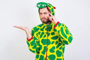 Fototapeta premium young caucasian man wearing a pajama standing against white wall confused and annoyed with open palm showing copy space and pointing finger to forehead. Think about it.