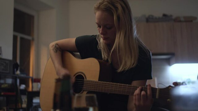 Pretty blonde girl playing guitar home in kitchen, house party