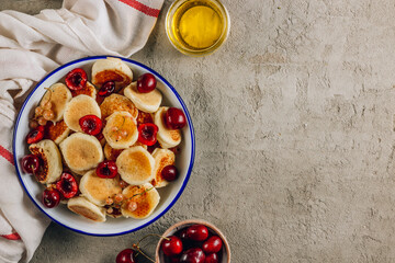 Trendy home breakfast with tiny pancakes, honey and cherries on a concrete table.